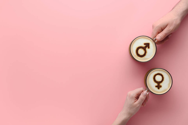 Manos de pareja enamorada sosteniendo tazas de café con símbolos de venus y marte sobre espuma de leche sobre fondo rosa pastel - Foto, Imagen