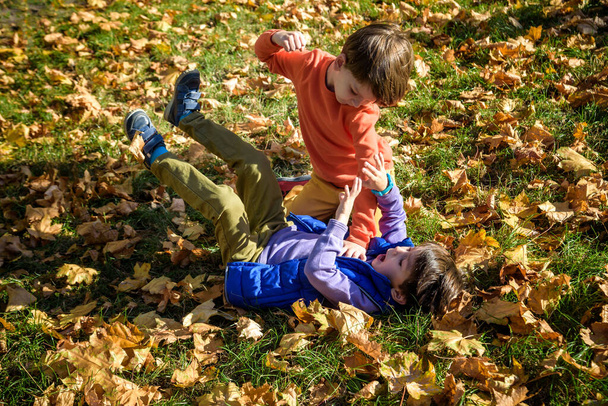 Two boys fighting outdoors. Friends wrestling in summer park. Siblings rivalry. Aggressive kid hold younger boy on ground, try to hit him. - Zdjęcie, obraz