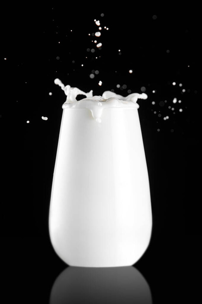 Splash σε ένα ποτήρι με γάλα απομονωμένο σε μαύρο φόντο - Φωτογραφία, εικόνα