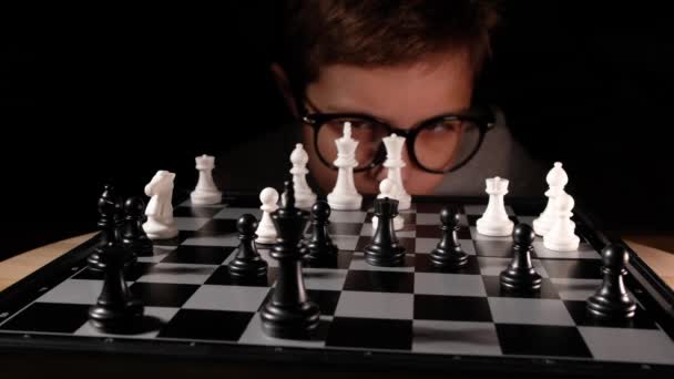 Niño jugando al ajedrez en la mesa. Niño con gafas desarrollando estrategia de ajedrez, jugar juego de mesa con un amigo. - Metraje, vídeo