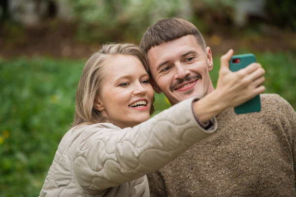 若い夫と妻は、緑の背景にソーシャルネットワーク上のブログのためのスマートフォンで一緒に自撮りを取ります。親密な感情. - 写真・画像