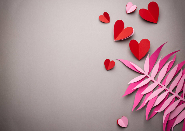 Cuori rossi tagliati di carta su sfondo rosa, carta artigianale stile origami, dall'alto. San Valentino romantico sfondo giorno e concetto di amore. Diverse dimensioni cuori rossi vista dall'alto, disegno arte della carta - Foto, immagini