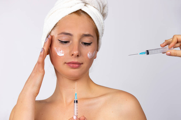 Cosmetological lifting injections and a pensive girl with a cream on her cheeks. Spa and skincare concept. High quality photo - Foto, Imagem