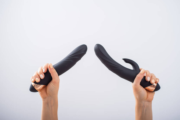 A faceless woman holds two black dildos on a white background - 写真・画像
