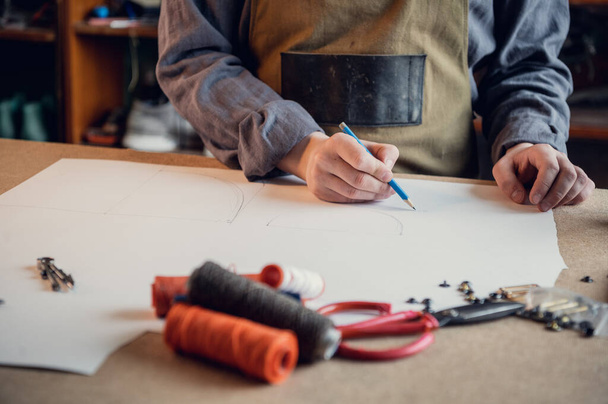 En una zapatería familiar un joven aprendiz trabaja con papel para crear un patrón para zapatos - Foto, imagen