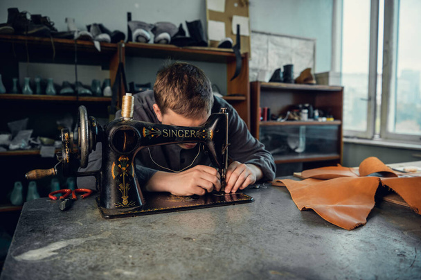 彼のワークショップで若い靴屋は、ミシンで革を縫う、注文する元の靴を作る - 写真・画像