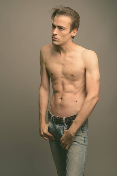 Studio shot of young handsome man shirtless against gray background - Foto, Imagem