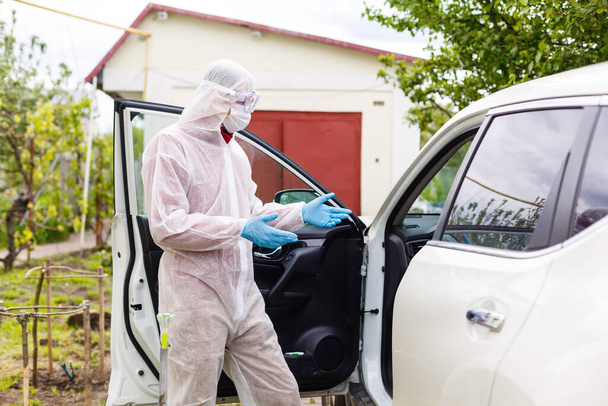 Mężczyzna w kombinezonie ochronnym dezynfekuje samochód po podczas nowego koronawirusa Covid-19. - Zdjęcie, obraz