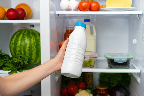 Female hand taking bottle of milk from a fridge - Фото, изображение