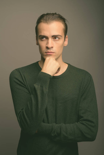 Studio shot of young handsome man wearing green long sleeved shirt against gray background - Foto, imagen