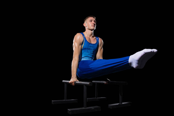 Muscular male gymnast training in gym, flexible and active. Caucasian fit guy, athlete in blue sportswear isolated on black - Photo, Image