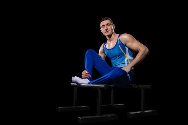 Muscular male gymnast training in gym, flexible and active. Caucasian fit guy, athlete in blue sportswear isolated on black - Photo, image