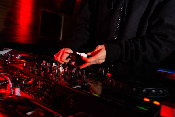 Male DJs hand turn tumblers and hold electronic cigarette. Close up shot. Nightlife concept. Man playing music at party in nightclub. Dark atmosphere. - Photo, Image