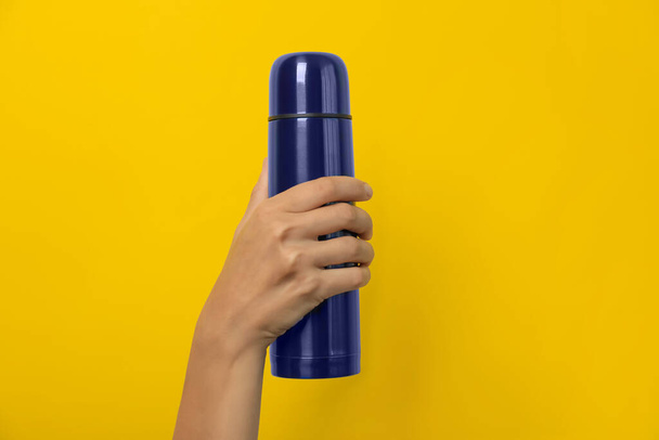 Woman holding modern blue thermos on yellow background, closeup - 写真・画像