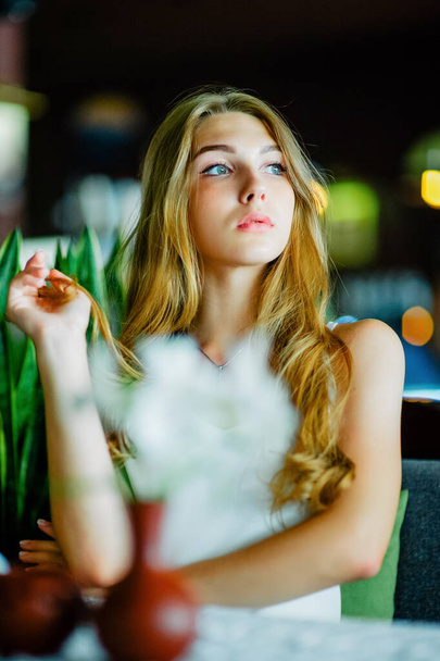 Дівчина з блакитними очима сидить у міському кафе. жінка з коричневою хвилястою зачіскою. Концепція стилю
. - Фото, зображення