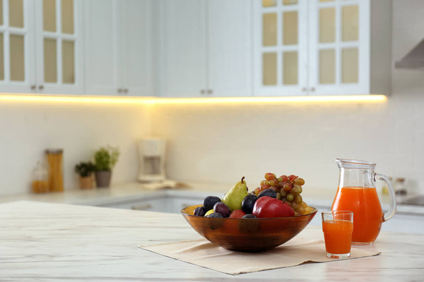 Different fresh fruits and juice on white table in modern kitchen. Space for text - Foto, Imagem