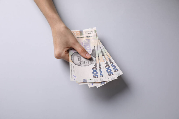 Γυναίκα κρατώντας τα ουκρανικά χρήματα σε ανοιχτό γκρι φόντο, closeup - Φωτογραφία, εικόνα