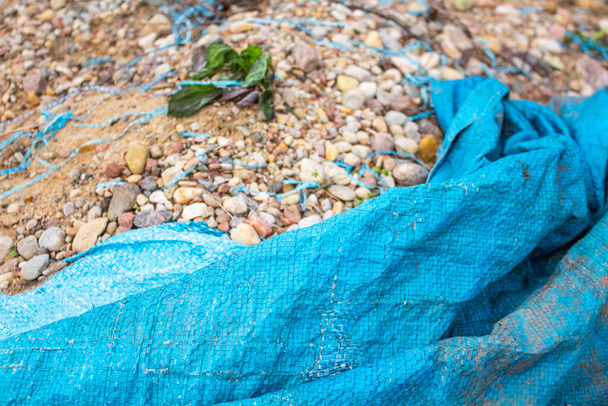 Blue tarp in the foreground sheltering a pile of sand and stones  - Фото, зображення