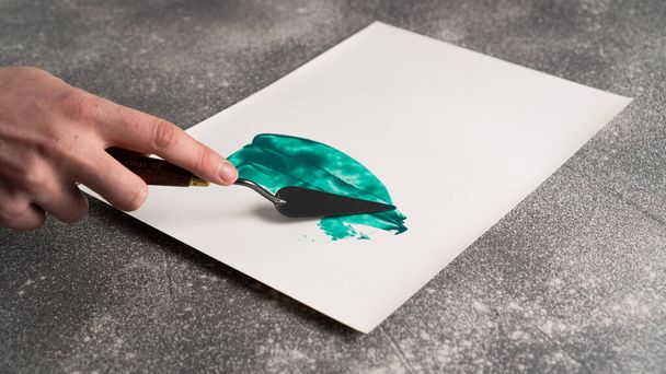 Χέρι κρατώντας πρότυπο μαχαίρι παλέτα και αφαίρεση ζωγραφική σε λευκό χαρτί. Μαχαίρι παλέτας - Φωτογραφία, εικόνα