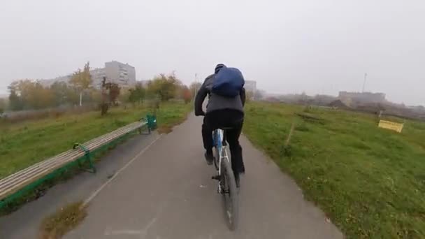 Parkta bisiklet sürmek. Sisli bir sabahta bir bisikletçi patika boyunca yol alır. Kamera onu takip ediyor ve arkasından yakalıyor. Sonbahar. - Video, Çekim