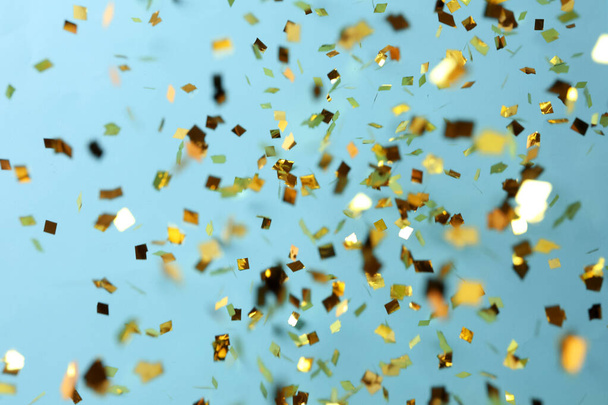 Shiny golden confetti falling down on light blue background - Photo, Image