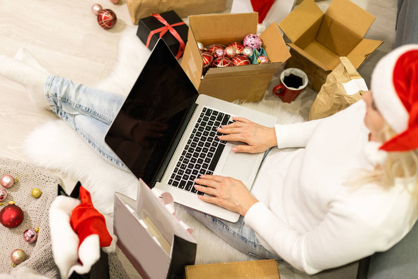Christmas online shopping top view. Female buyer with laptop, copy space on screen. Woman has coffee, buys presents, prepare to xmas eve, sitting among gifts boxes and packages. Winter holidays sales - Photo, Image