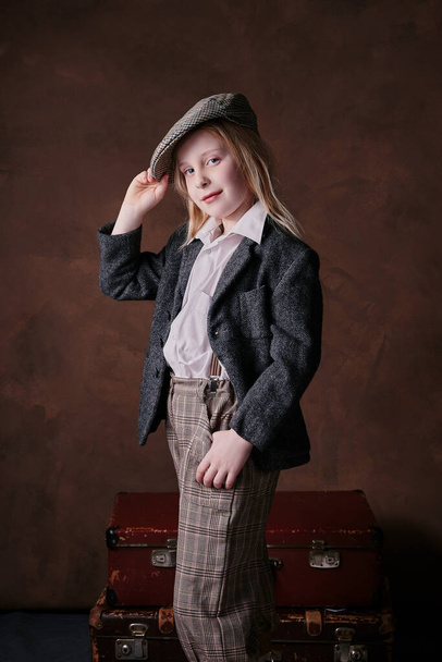 retro portrait of a little girl in a cap with a visor. suit jacket and pants. brown background - Фото, зображення