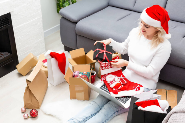 Christmas online shopping top view. Female buyer with laptop, copy space on screen. Woman has coffee, buys presents, prepare to xmas eve, sitting among gifts boxes and packages. Winter holidays sales - Fotografie, Obrázek