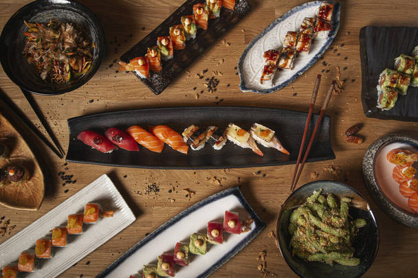 Bild mit verschiedenen Gerichten aus Sushi, Sashimi, Nigiri, Yakisoba und Edamame auf dem Restauranttisch - Foto, Bild