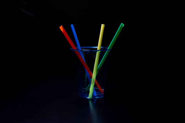 黒の背景にプラスチック製のカップに4色の飲料プラスチックストロー - 写真・画像