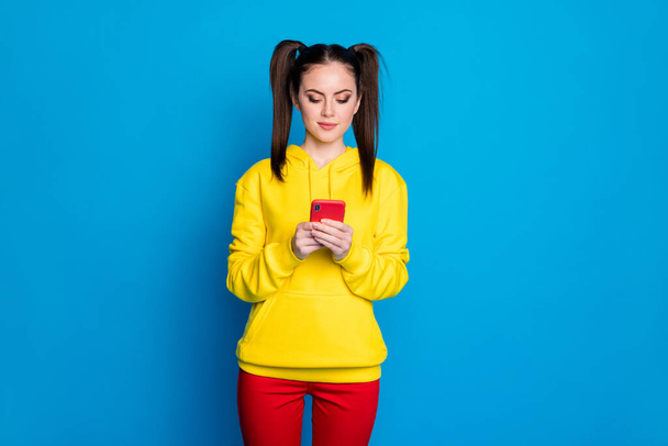 Photo of attractive charming lady two tails hold browsing telephone popular blogger writing new post wear casual yellow hoodie red trousers isolated bright blue color background - Foto, afbeelding