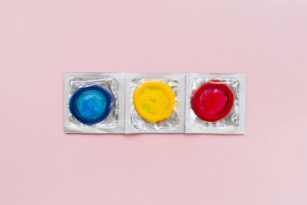 Composition with colorful condoms on pastel pink background. Safe sex and contraceptive concept. Flat lay, top view, copy space - Fotó, kép