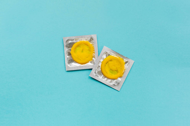 Kolorowa kompozycja z żółtymi prezerwatywami na jasnoniebieskim tle. Bezpieczny seks i antykoncepcja. Płaskie ułożenie, widok z góry, przestrzeń do kopiowania - Zdjęcie, obraz