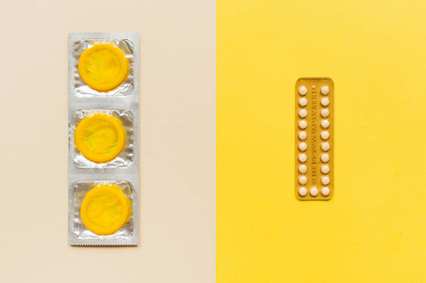 Composition with colorful condoms and birth control pills on yellow background. Safe sex and contraceptive concept. Flat lay, top view, copy space - Photo, image