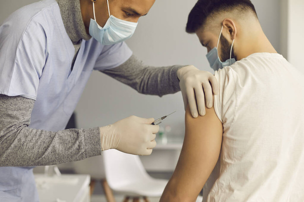 Médico en mascarilla facial inyectando a paciente con vacuna antiviral durante campaña de inmunización - Foto, imagen
