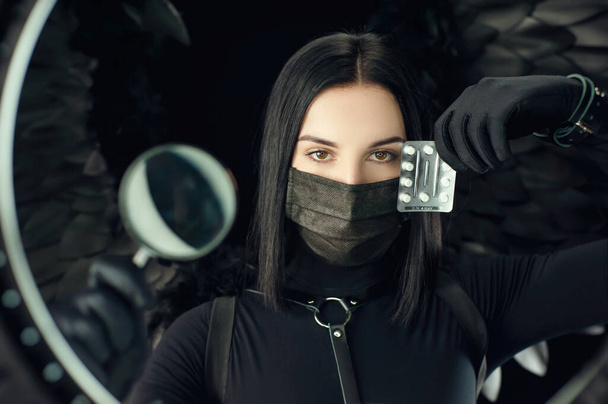 брюнетка в защитной черной коронавирусной маске с таблетками и увеличительным стеклом - Фото, изображение
