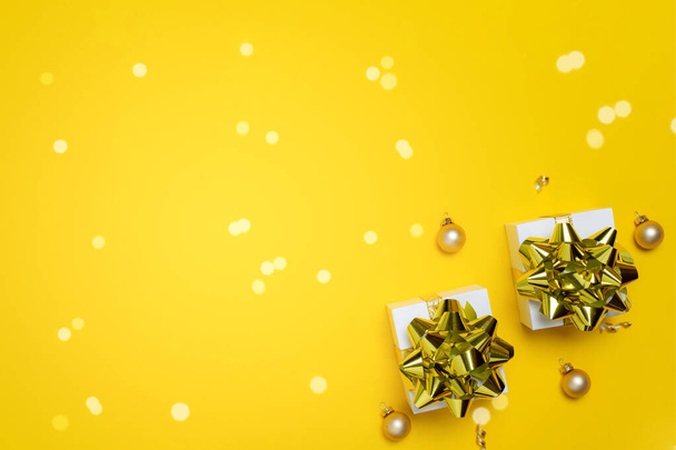 Świąteczne tło. Białe pudełko z wstążką w kolorze złotym, piłki noworoczne i błyszczące światła w składzie xmas na ciemnożółtym kartce okolicznościowej. Odbiór. Zimowe wakacje, Nowy Rok - Zdjęcie, obraz