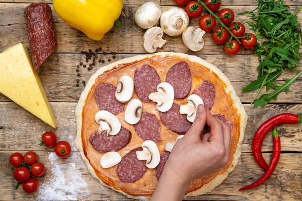 Ingredients for making pizza, before baking, on a wooden table, top view hand laid out mushrooms, step-by-step recipe. High quality photo - Photo, Image