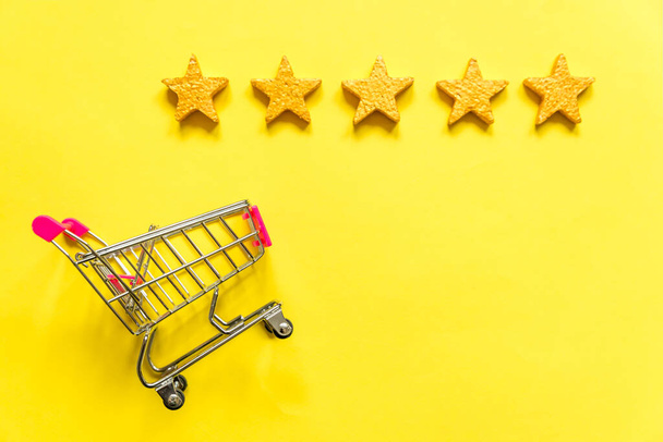 単にフラットレイデザイン黄色の背景に隔離された車輪と5つの金の星の評価で買い物のための小さなスーパーマーケットの食料品プッシュカート。小売消費者オンライン評価とレビューの概念を購入 - 写真・画像