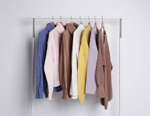 Warm sweaters hanging on rack against white background - Foto, Bild