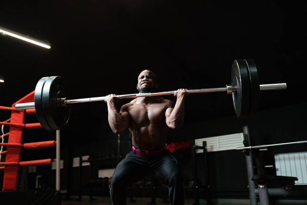 Heavyweight man training with a barbell. Bodybuilding trainer lifts heavy weights in the gym, preparing for competition - Foto, Imagem