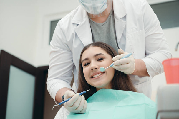 Kaunis tyttö hymyilee, kun lääkäri tutkii leukansa hammaspinseteillä. terveet hampaat käsite - Valokuva, kuva