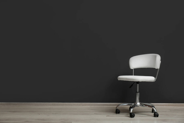 Comfortable office chair near black wall indoors. Space for text - Foto, afbeelding