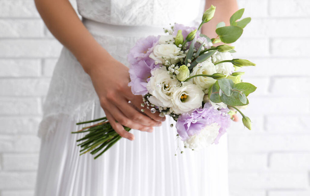 Bruid met prachtig boeket met Eustoma bloemen in de buurt van bakstenen muur, close-up - Foto, afbeelding
