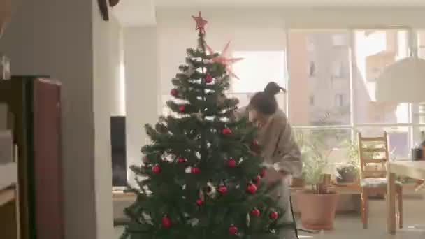 Donker haar gemengd ras meisje versieren en kunstmatige kerstboom thuis. Medium Wide Camera shot 4k videobeelden van hoge kwaliteit. - Video