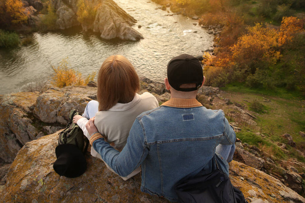 Couple of hikers with travel backpacks sitting on steep cliff, above view - Foto, imagen