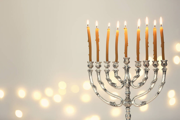 Silver menorah with burning candles against light grey background and blurred festive lights, space for text. Hanukkah celebration - Foto, Imagen
