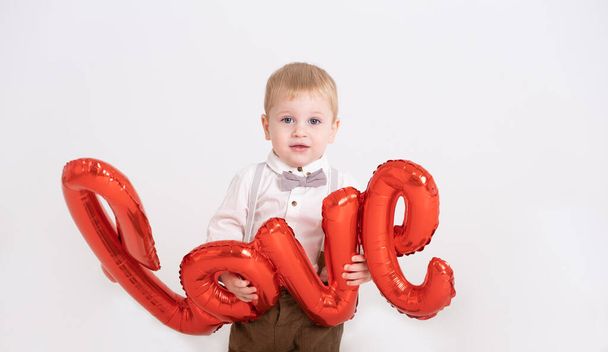 bébé tout-petit garçon en costume tient l'amour de l'inscription de ballons sur un fond blanc - Photo, image
