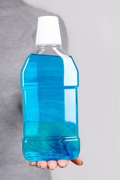 Hand with blue mouthwash on grey. - Foto, Imagen