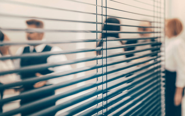 through the blinds. company employees in the workplace in the office. - Foto, immagini